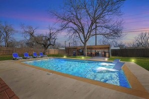 Une piscine rectangulaire avec une terrasse en bois, entourée de chaises longues bleues.