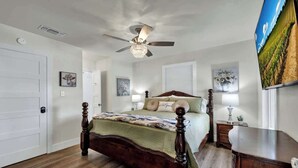 A bedroom with a wooden bed, a ceiling fan, and a wall-mounted TV.