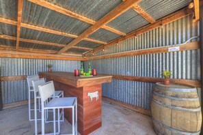 A rustic bar area with a wooden counter, metal chairs, and a barrel. - Crystal Cow Haus Luxury Home-Pool-HotTub-Near Main (Fredericksburg)