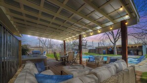 An outdoor patio with a covered seating area, a pool, and a barbecue setup.