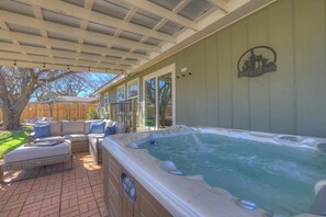 Un espace avec un jacuzzi, doté d’un patio couvert, de sièges extérieurs et d’une clôture en bois en arrière-plan.