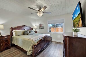 Une chambre à coucher avec un lit en bois, un ventilateur de plafond, une télévision et une fenêtre donnant sur une clôture.