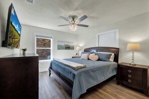 Une chambre à coucher avec un lit, un ventilateur de plafond, une télévision, une fenêtre et une table de chevet.