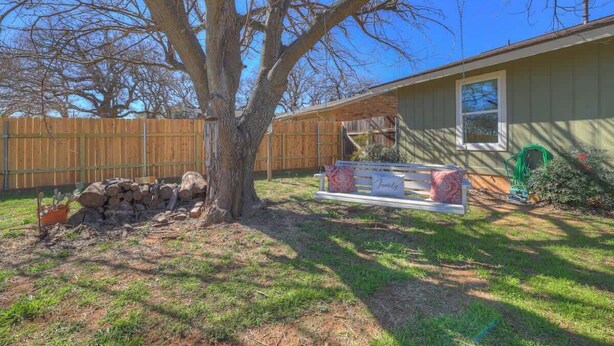 Un patio trasero con un árbol grande, cerca de madera, un banco y una casa.