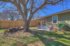 A backyard with a large tree, a wooden fence, a bench, and a house. - Crystal Cow Haus Luxury Home-Pool-HotTub-Near Main (Fredericksburg)