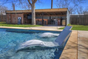 A pool with a wooden deck and a building with a covered patio area. - Crystal Cow Haus Luxury Home-Pool-HotTub-Near Main (Fredericksburg)