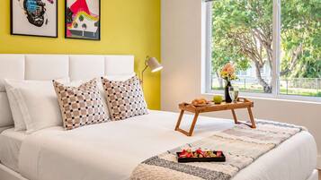 Een bed met witte lakens, geruit kussens en een dienblad met snacks.