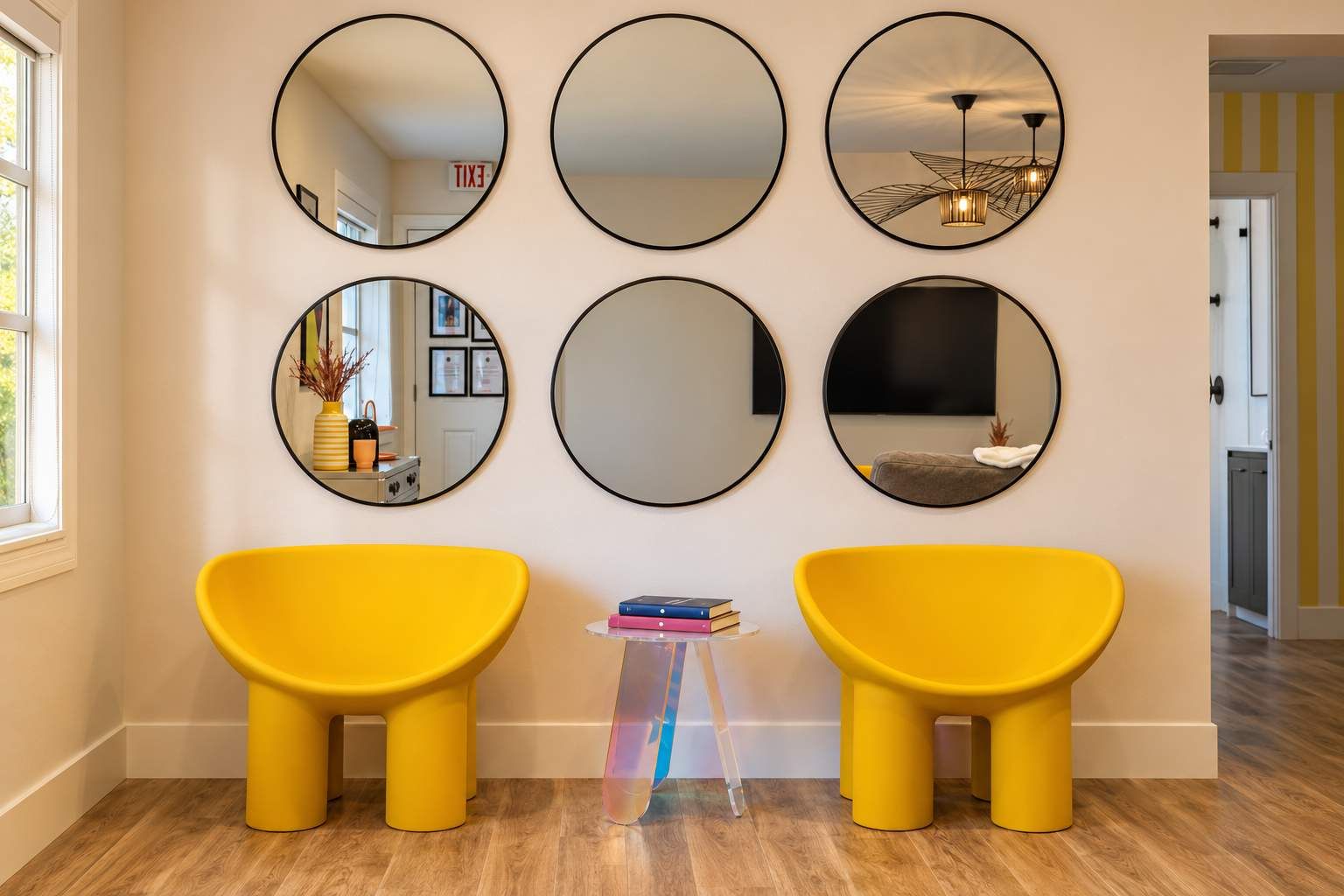 Ein Zimmer mit sechs runden Spiegeln an der Wand, zwei gelben Stühlen und einem kleinen Tisch mit Büchern.