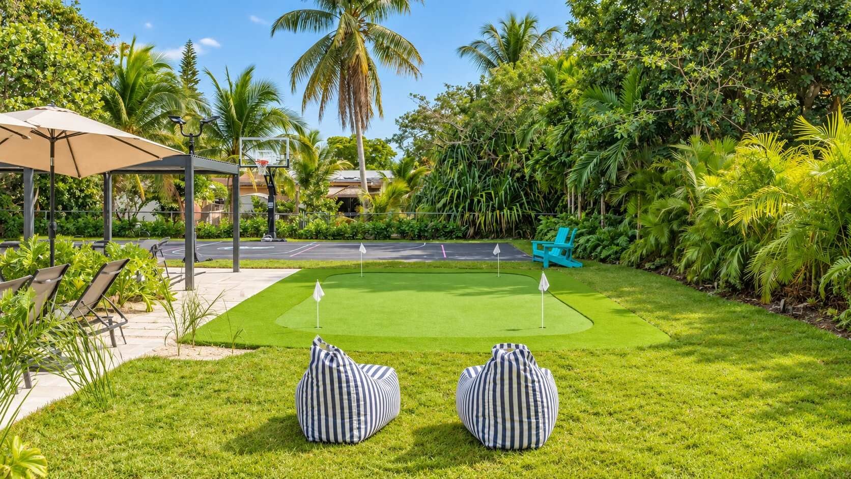 Een verzorgd gazon met een putting green, twee gestreepte ligzakken, een blauwe stoel en een prieel.