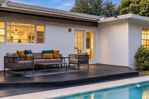 A poolside area with a sofa and chairs, a small table, and a pool.