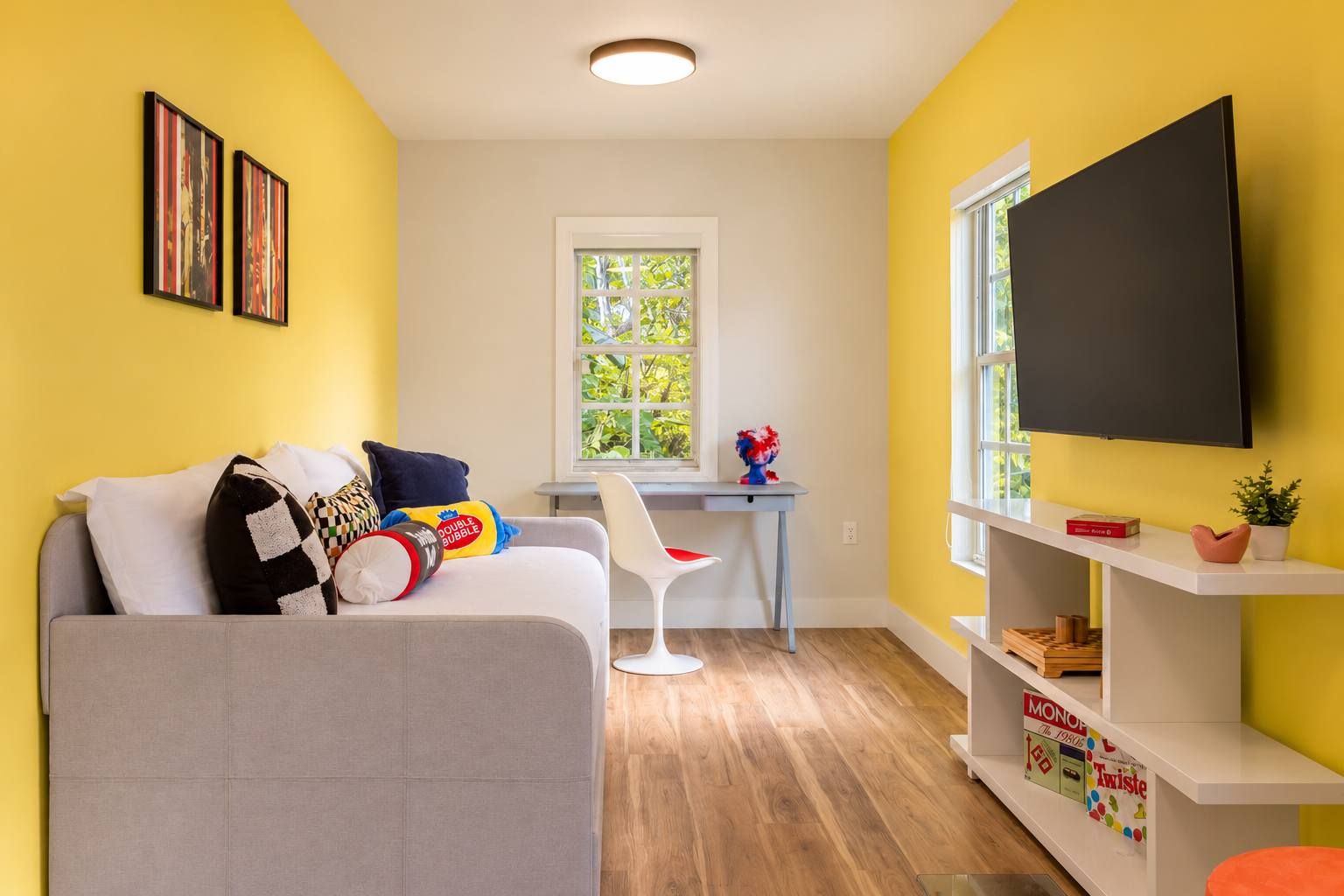 Ein modernes Wohnzimmer mit einem grauen Sofa, einem weißen Sessel, einem kleinen Tisch und einem an der Wand befestigten Fernseher.