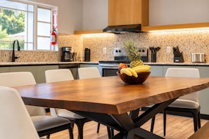 A modern kitchen with a wooden dining table, white chairs, and a fruit bowl on the table.