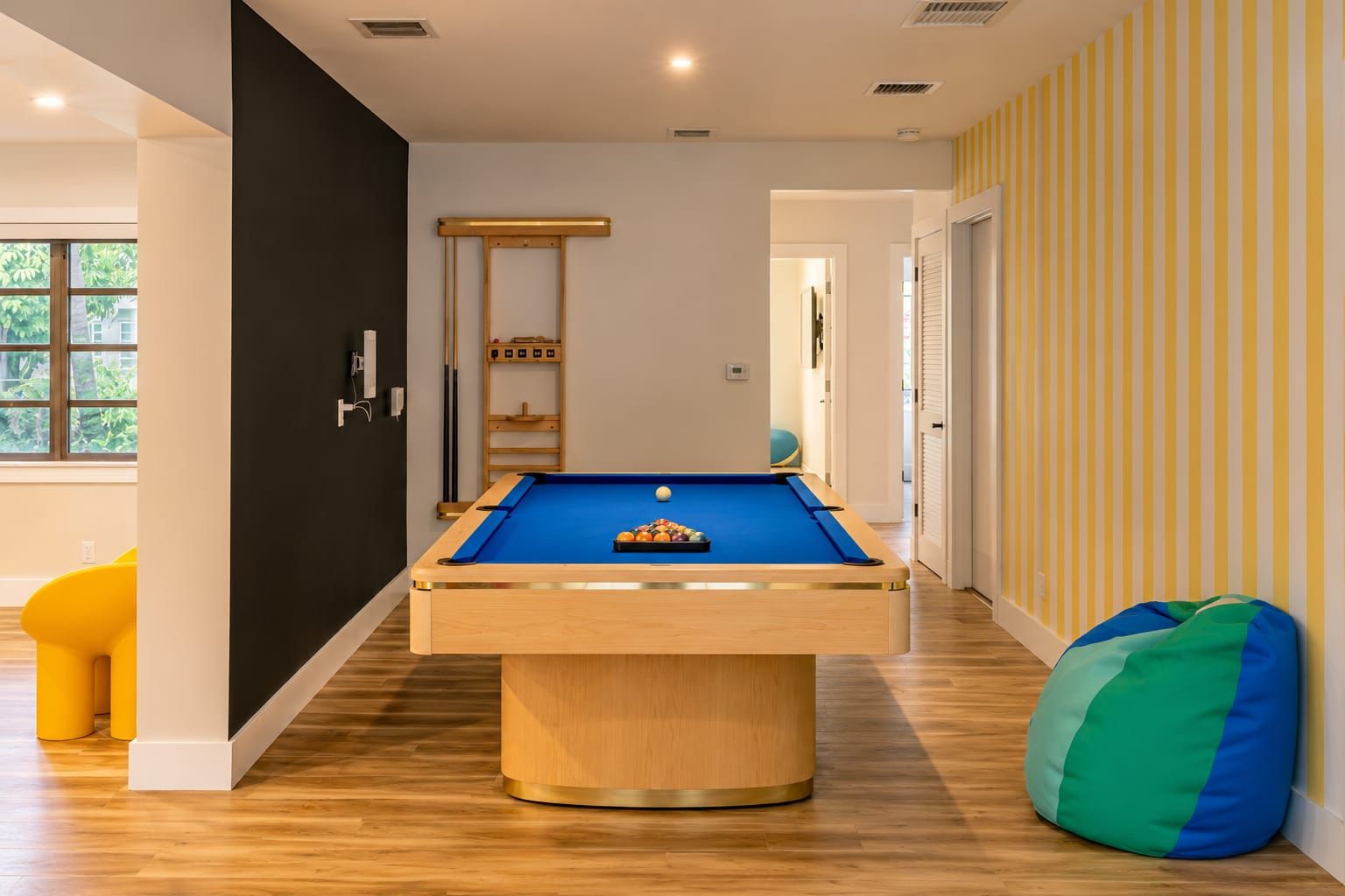 Ein Billardtisch in einem Raum mit Holzboden, schwarzer Wand und Streifenmuster.