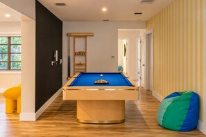 A pool table in a room with wooden flooring, a black wall, and a striped wall.