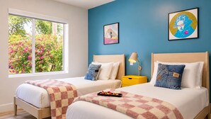 Une chambre avec deux lits, une fenêtre donnant sur un paysage verdoyant et un mur orné de deux tableaux encadrés.
