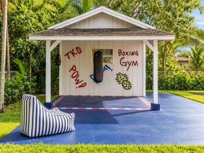 Ein kleines Gebäude, an dem 'Boxing Gym' steht, mit einem Sandsack und einer blauen Matte mit roten und weißen Markierungen.