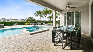 Un espace aménagé au bord de la piscine, avec une table et des chaises, un ventilateur de plafond et une vue sur les maisons voisines.