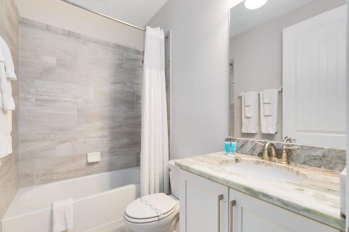 A modern bathroom with a shower, toilet, and vanity with a marble countertop.