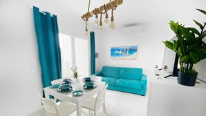 Un salon lumineux et moderne, avec un canapé turquoise, une table à manger dressée avec des assiettes et des verres, et un luminaire suspendu.