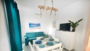 Un coin repas avec une table blanche dressée pour quatre personnes, des coussins turquoise et un canapé turquoise.