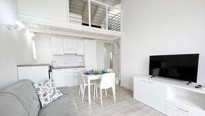 A modern, white-themed living area with a sofa, a dining table, and a TV. - Affittimoderni Castelsardo The Sun - CSSO11 (Castelsardo)