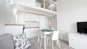 A modern, white-themed apartment with a dining area, kitchenette, and a TV on a cabinet. - Affittimoderni Castelsardo The Sun - CSSO11 (Castelsardo)