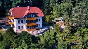 A multi-story building with a red roof, surrounded by dense forest.