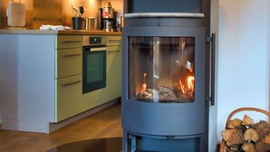 A modern kitchen with a built-in wood stove, a coffee maker, and a basket of firewood.