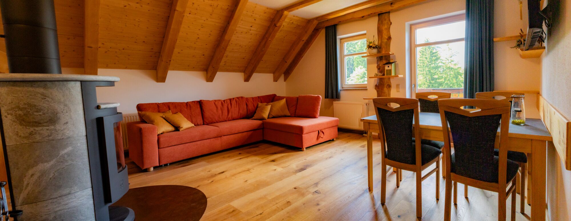 Une pièce chaleureuse avec un plafond en bois, un canapé rouge, une table à manger avec des chaises et une cheminée.