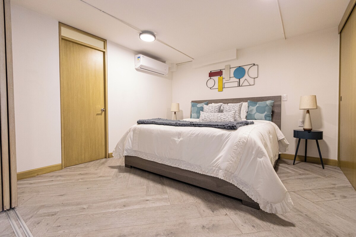 A bedroom with a bed, bedside lamps, a wall-mounted air conditioner, and a door.