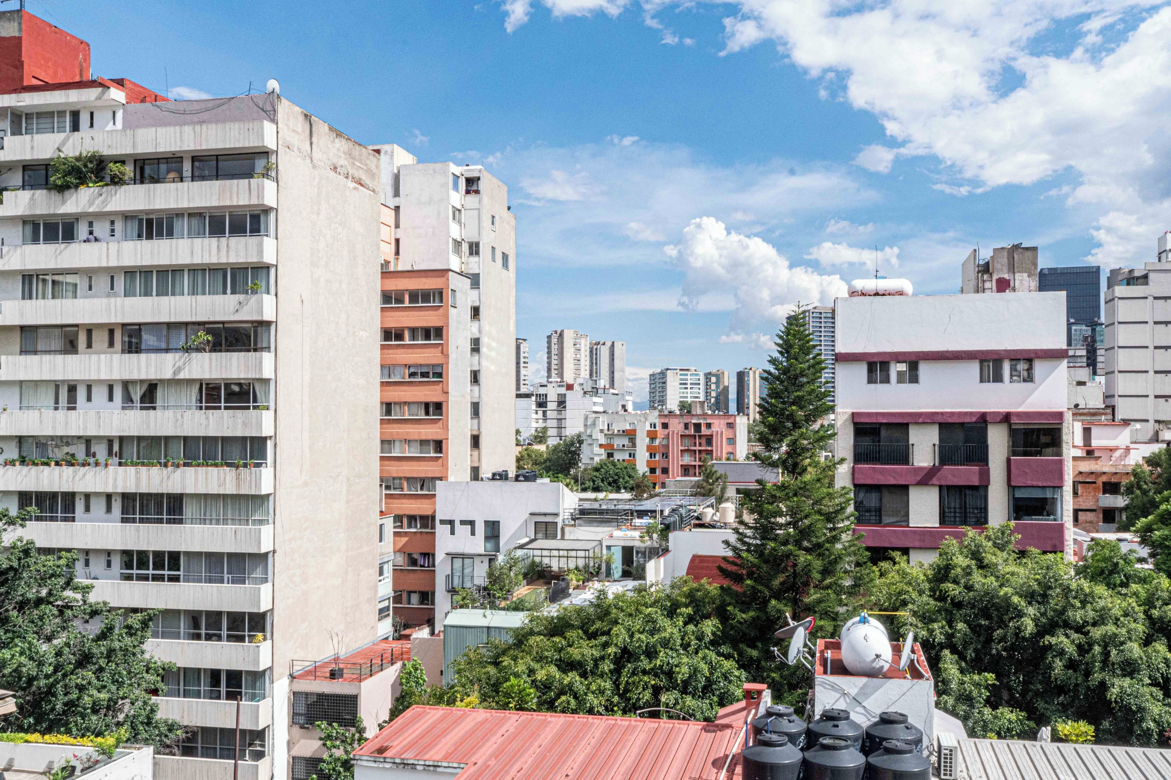 A multi-story building with balconies, a rooftop with satellite dishes, and a dense urban background.
