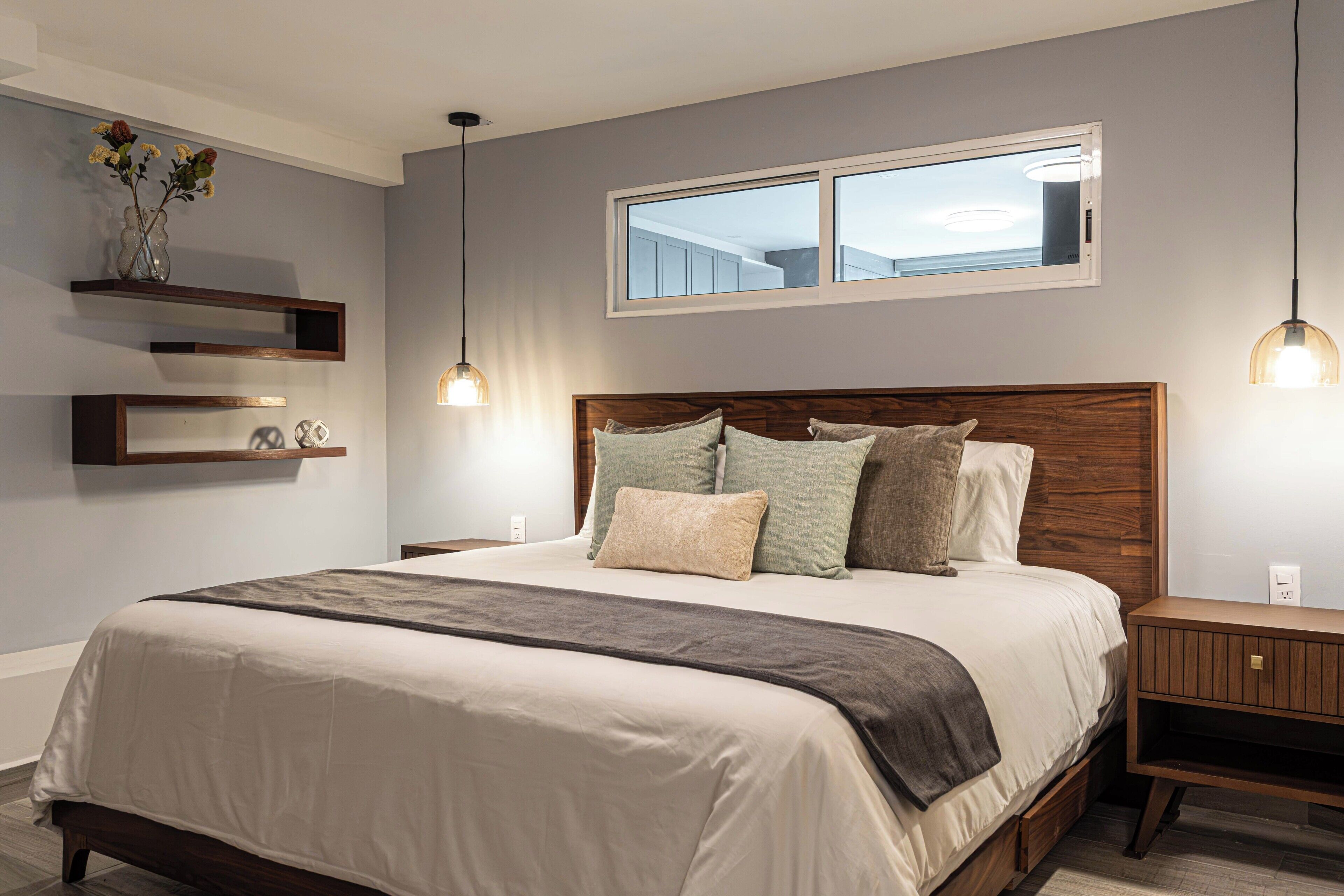A modern bedroom with a large bed, bedside tables, a window, and pendant lighting.