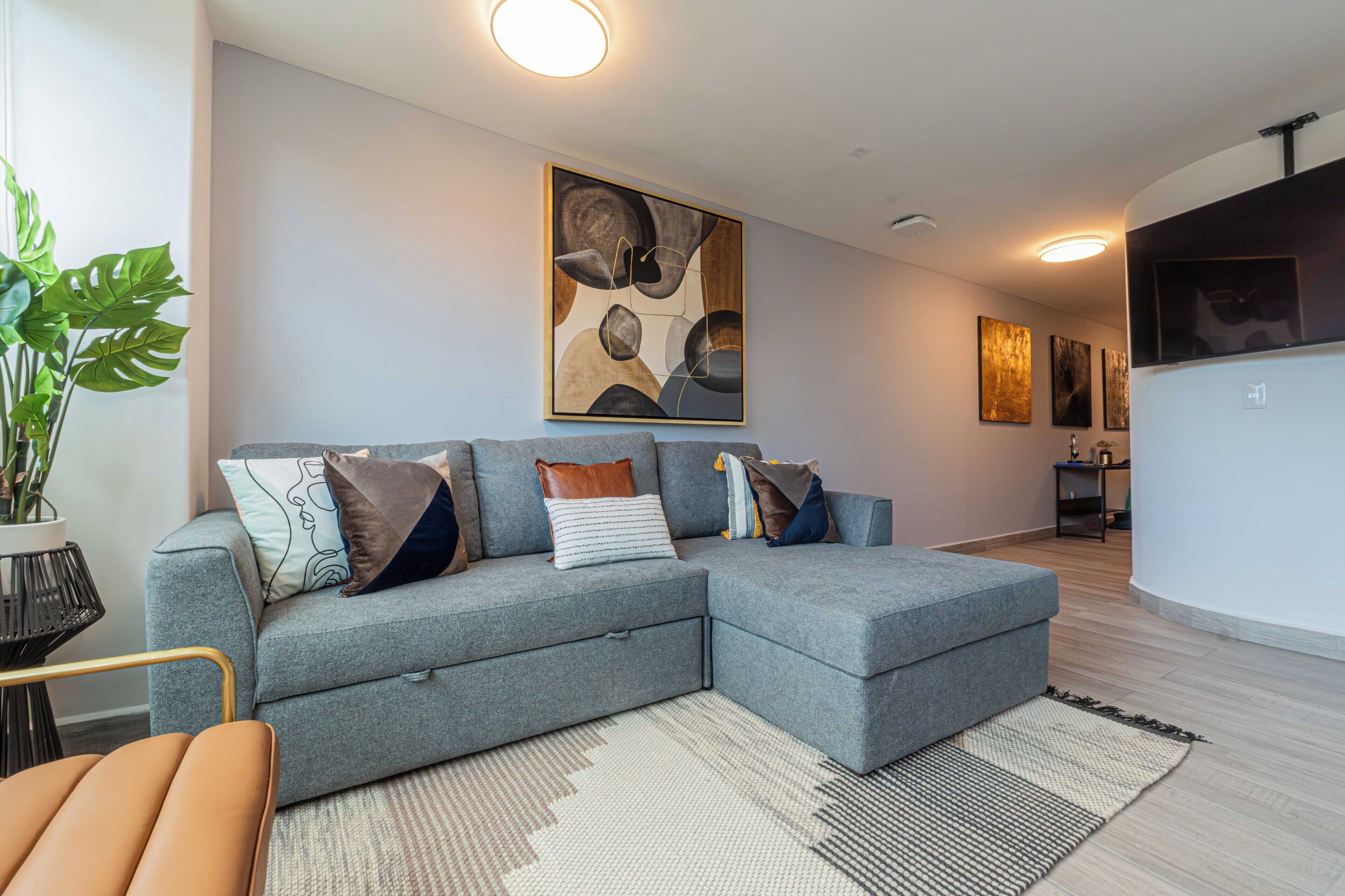 A modern living room with a grey sectional sofa, a potted plant, and abstract wall art.