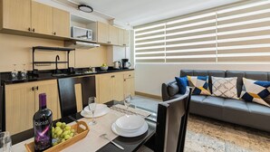 A modern living room with a grey sofa, a dining table set with plates, glasses, and a bottle of wine. There is a kitchen area with wooden cabinets and a microwave. - Apartments Homero 538 (Mexico City)