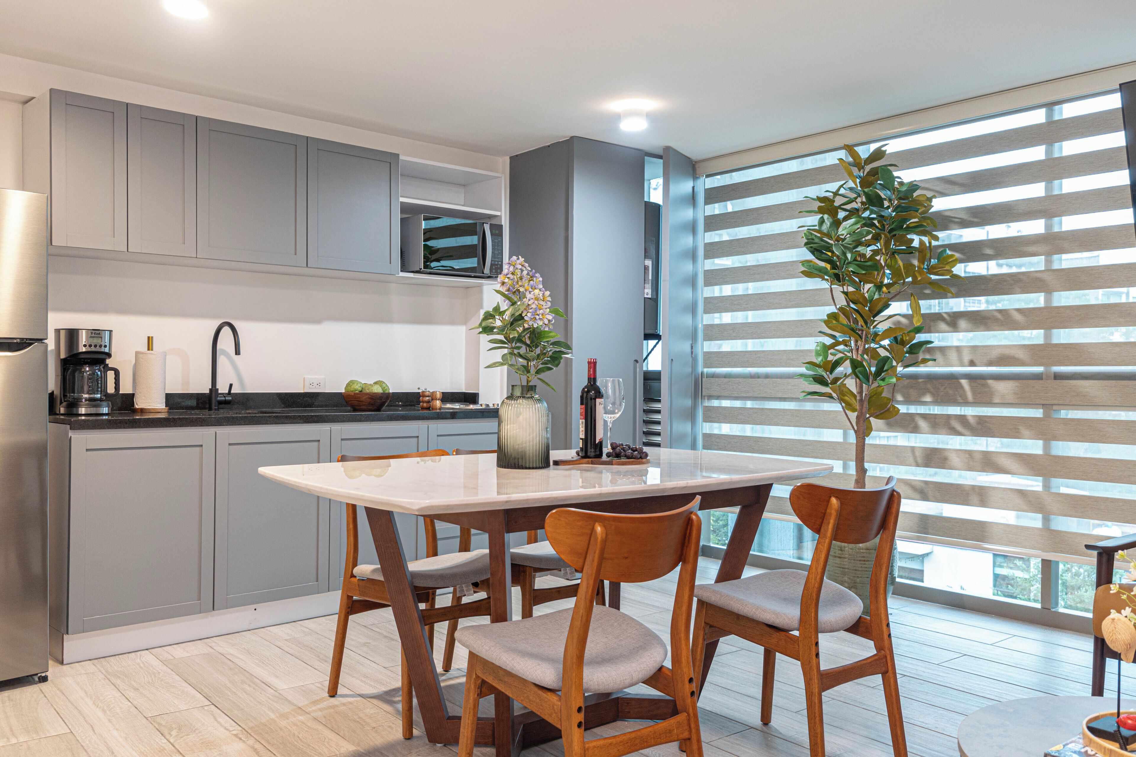 A modern kitchen with grey cabinets, a built-in microwave, and a dining area with a white table and wooden chairs.