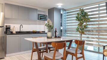 A modern kitchen with grey cabinets, a built-in microwave, and a dining area with a white table and wooden chairs.