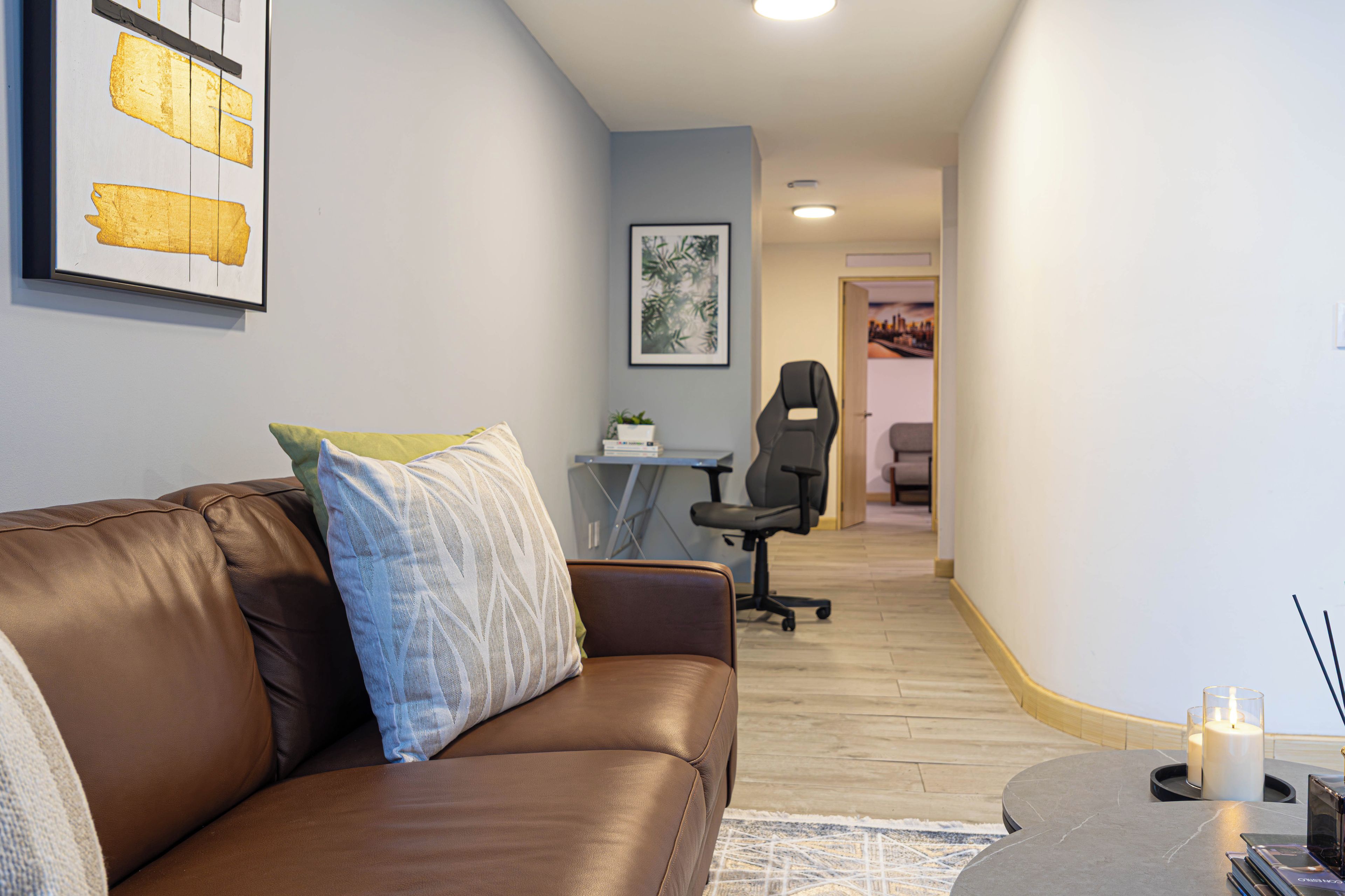 A modern living room with a leather sofa, a small coffee table, and a desk with a chair.