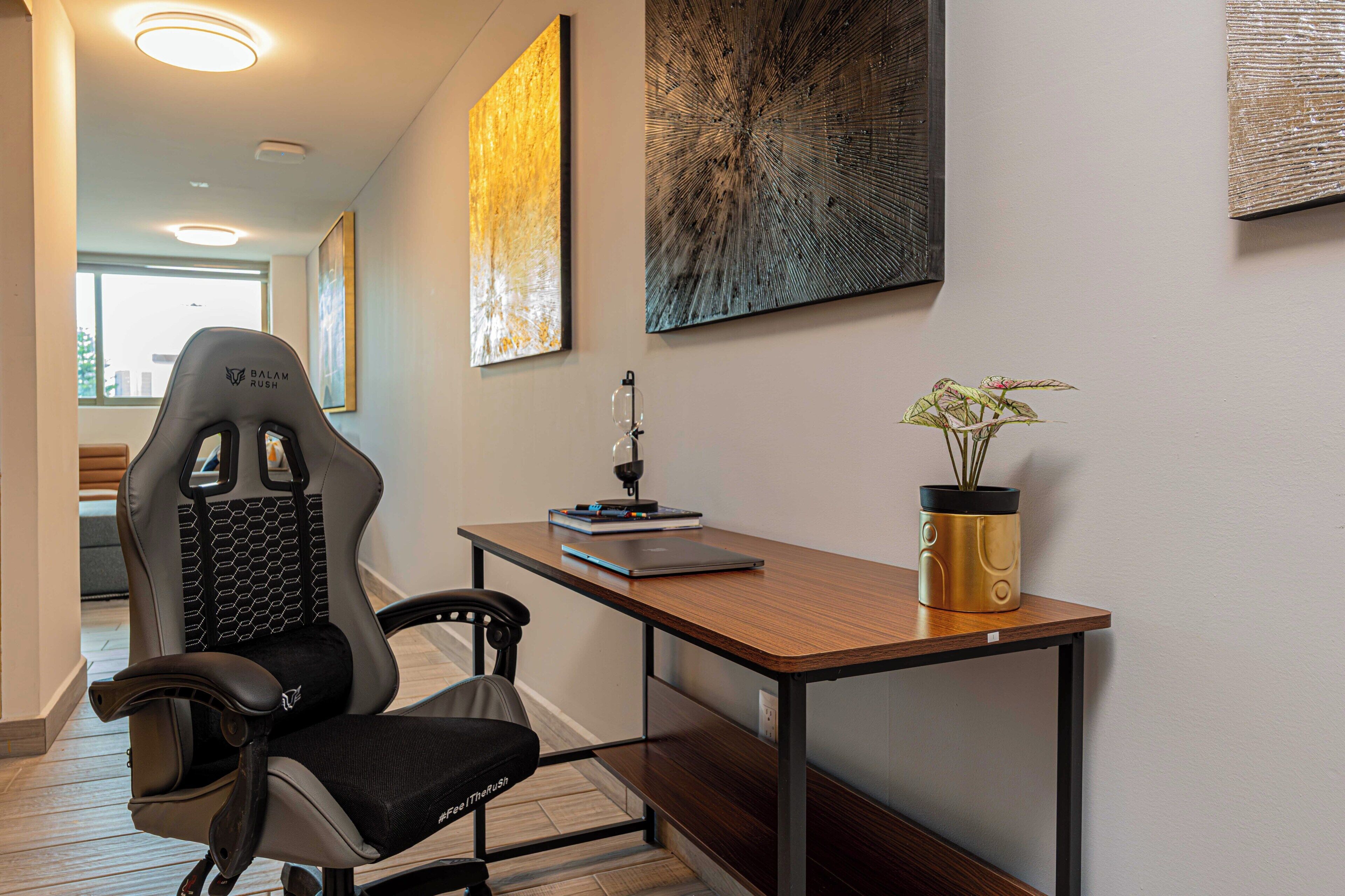 A modern office space with a high-backed ergonomic chair, a wooden desk with a laptop, a potted plant, and abstract wall art.
