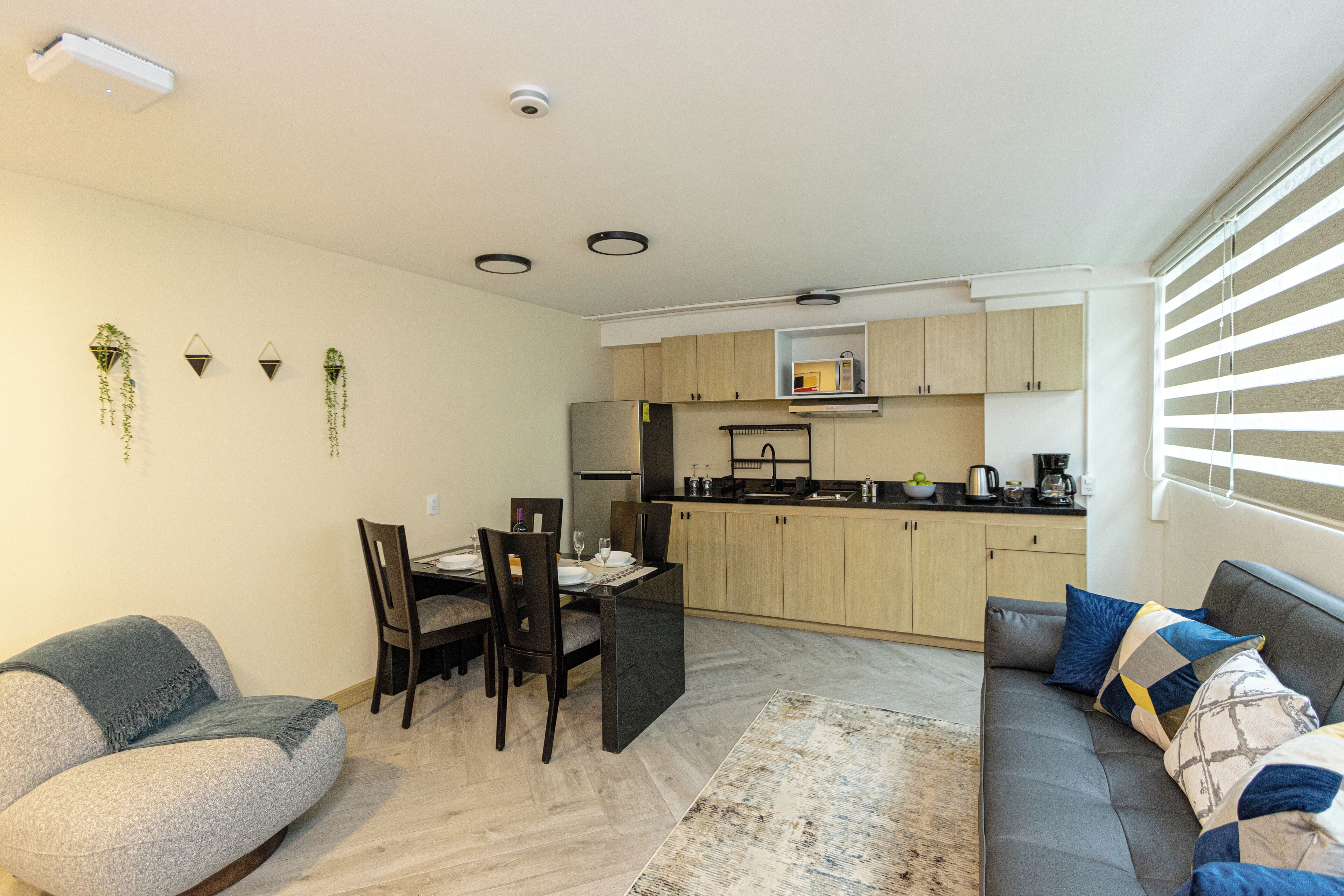 Sala de estar moderna com sofá, mesa de jantar e cadeiras. Há uma área de cozinha com armários e eletrodomésticos.