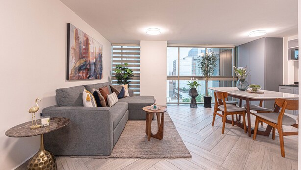 A modern living room with a grey sofa, a small round table, and a dining area with wooden chairs. - Apartments Homero 538 (Mexico City)