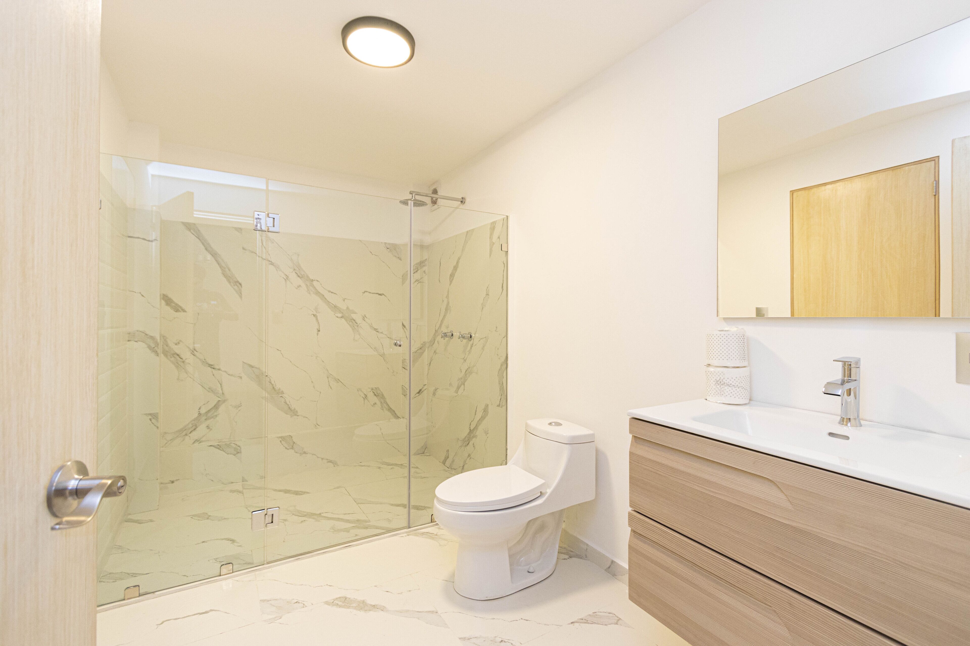 Et moderne badeværelse med en glasbrusekabine, toilet og et spejl med underskab.