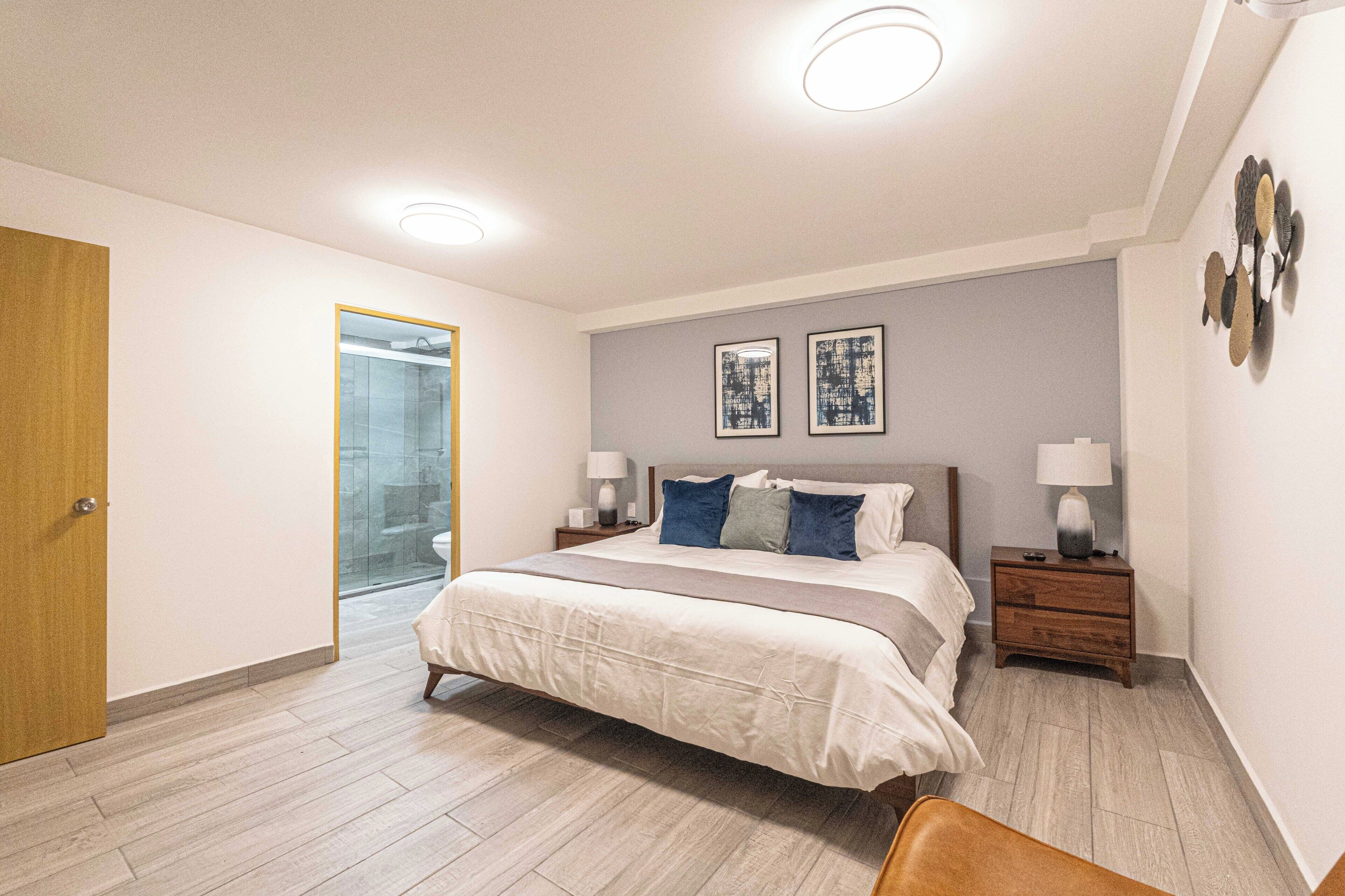 A modern bedroom with a large bed, bedside tables, and a glass shower door.