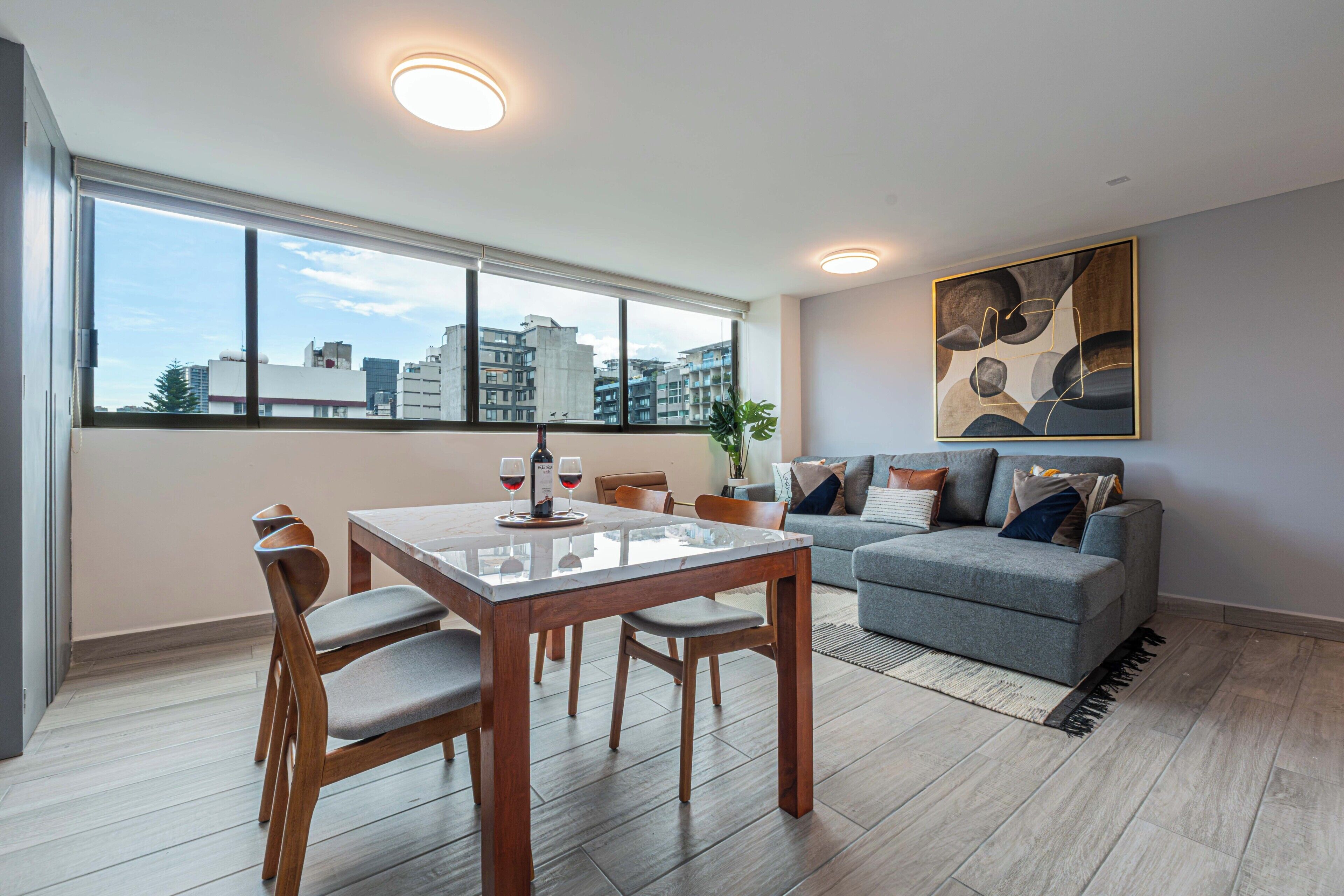 Un moderno salón con una mesa de comedor, asientos, un sofá y un ventanal con vistas a la ciudad.