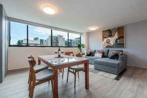 A modern living room with a dining table, seating, a sofa, and a large window with a city view. - Apartments Homero 538 (Mexico City)