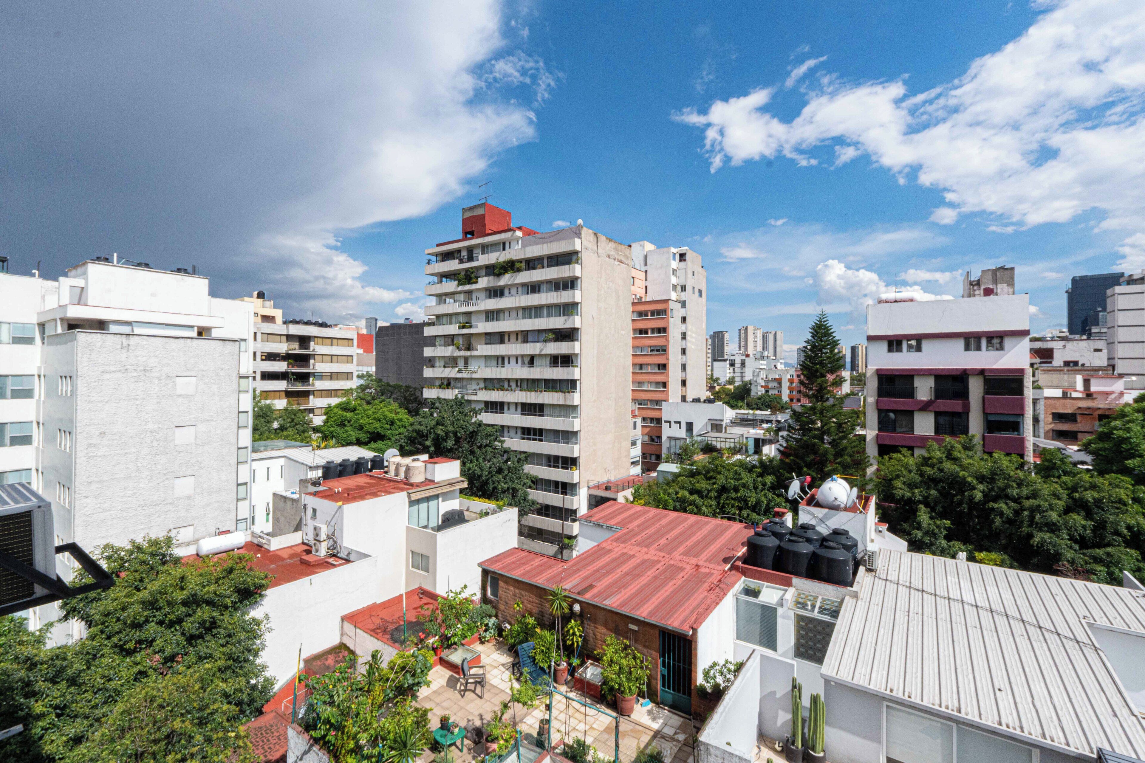 Un edificio alto con varios balcones, rodeado de otros edificios y vegetación.