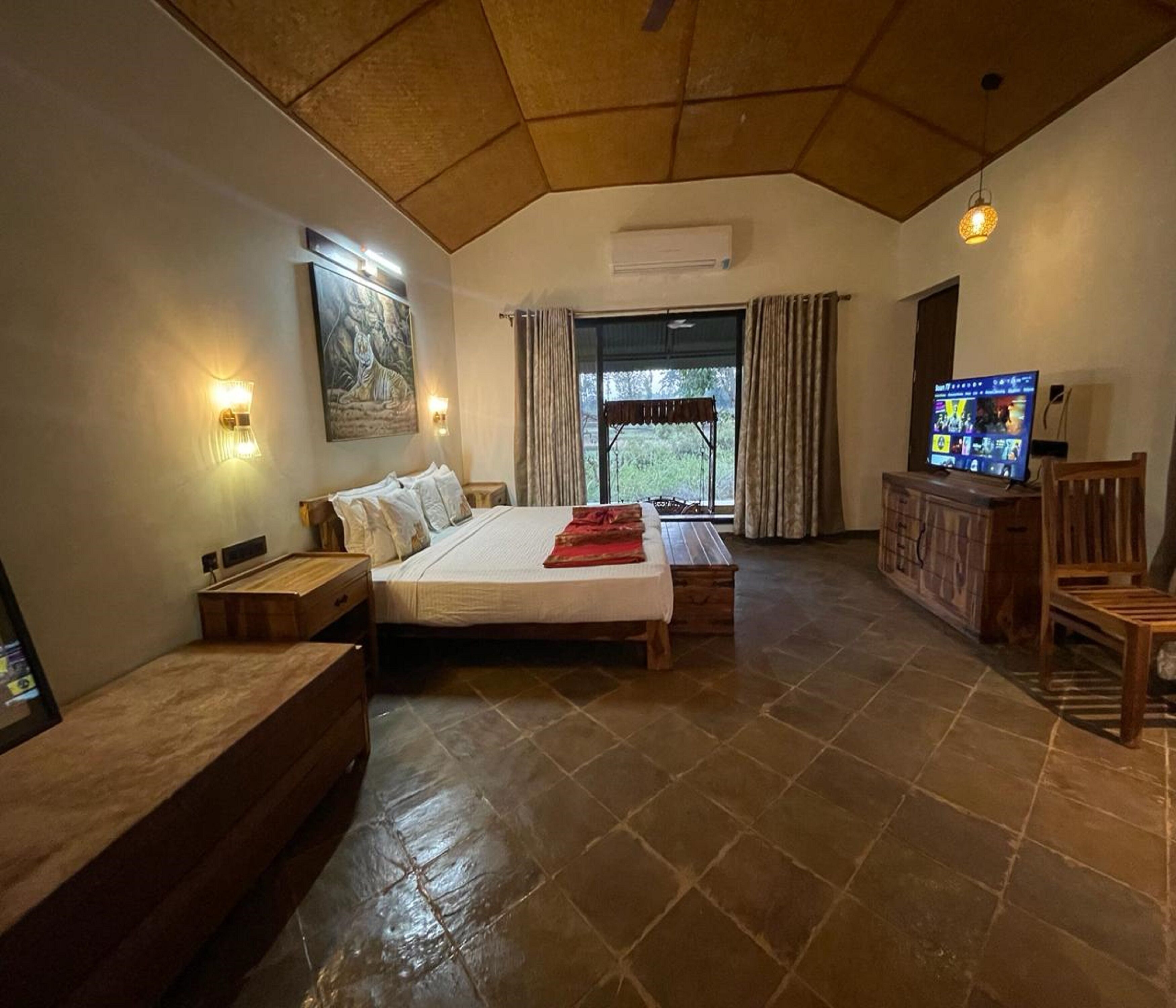 Un dormitorio con una cama grande, un banco de madera, un televisor y una ventana con cortinas.