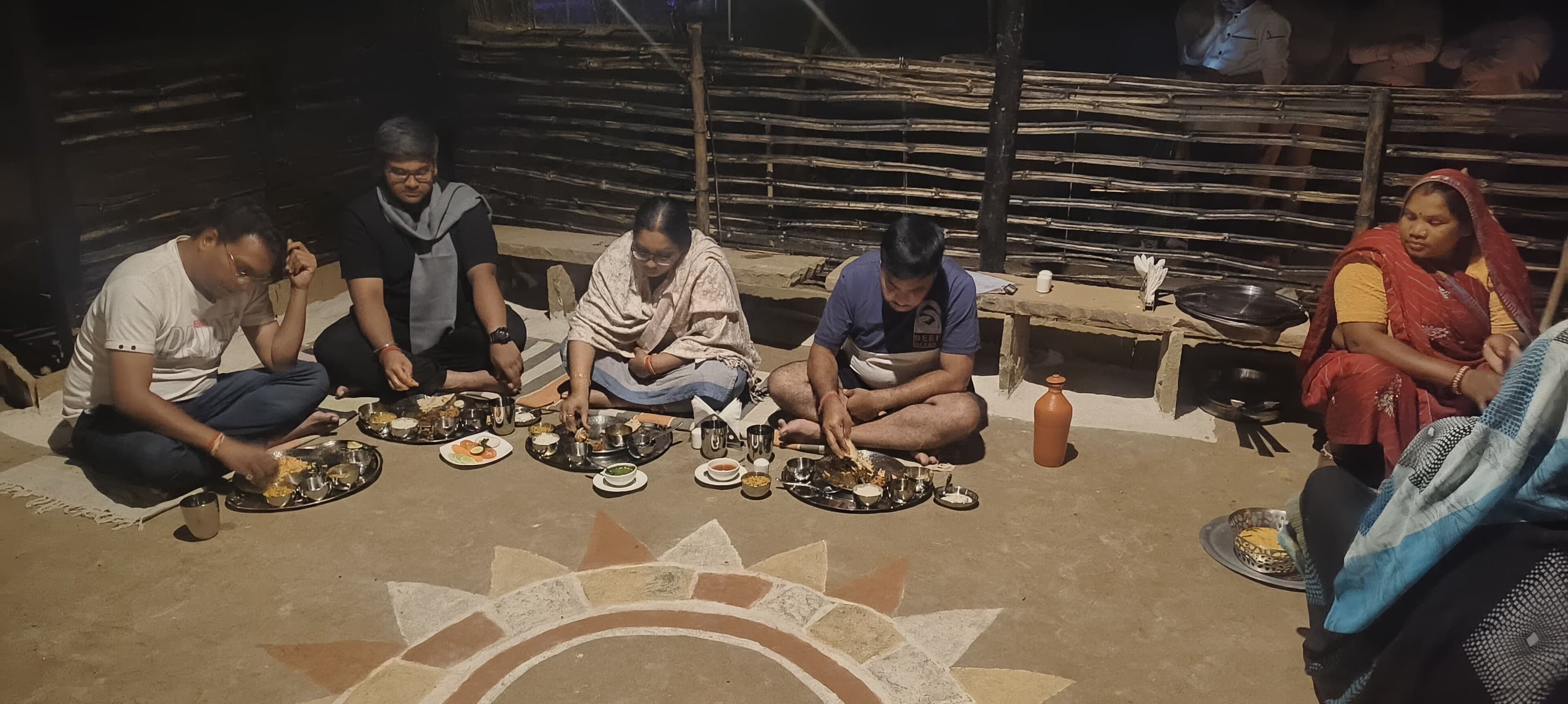 A group of people seated on the floor, sharing a meal with various dishes and utensils.