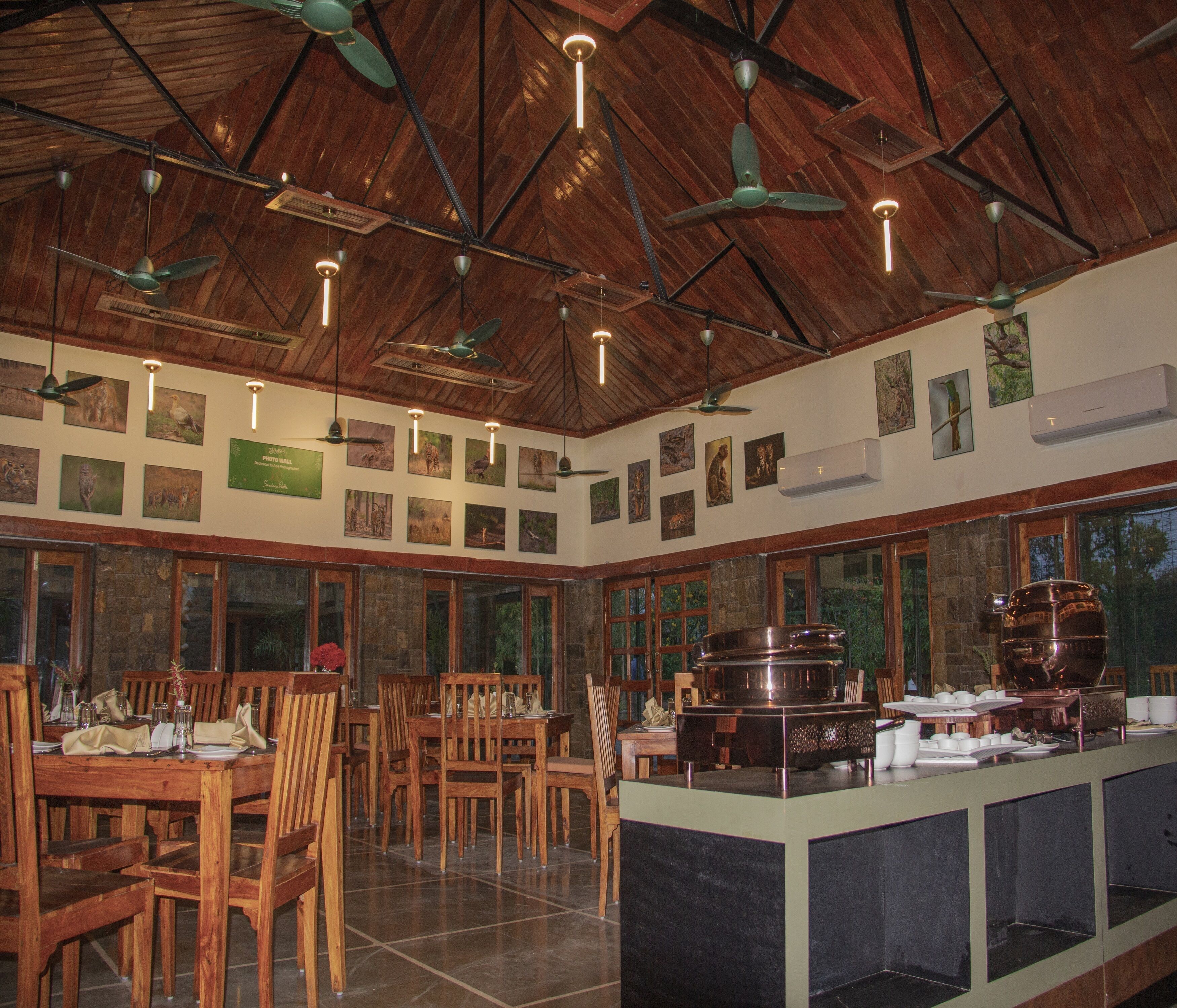 A restaurant with wooden ceiling fans, large windows, and a central serving area with a large pot.