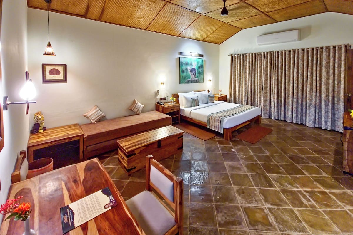 A hotel room with a bed, a desk, a chair, a wooden bench, a dining table, and a tiled floor.