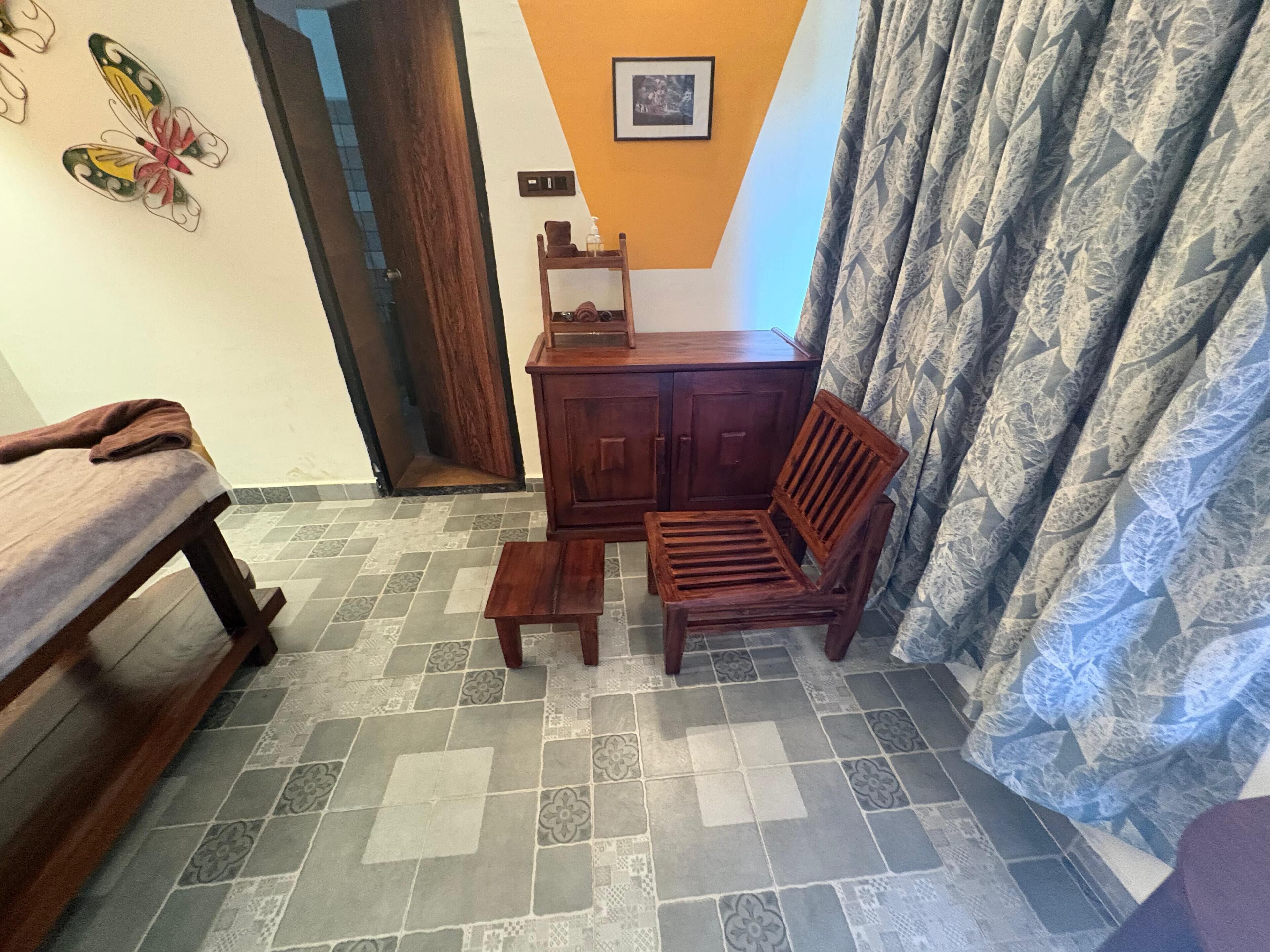 A room with a wooden bench, a small table, a wooden chair, a cabinet, and patterned curtains.